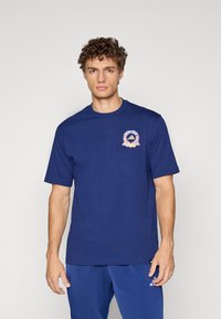 Marineblå bomulds t-shirt med korte ærmer, prydet med en rund halsudskæring og et flerfarvet rundt logo på venstre bryst.