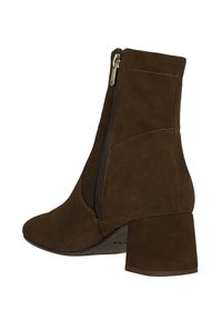 Bottine en daim marron avec une fermeture éclair sur le côté, un talon carré et un bout pointu ; elle présente des coutures discrètes et une texture lisse.