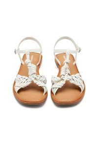 Sandali flat bianchi con cinturini intrecciati e fibbia alla caviglia. Soletta in pelle color tan con una texture liscia. Design open-toe.