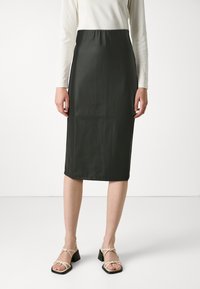 Jupe crayon noire, longueur genoux, fabriquée dans un tissu lisse avec une silhouette ajustée. Portée avec des sandales légères à lanières beiges avec un talon carré.