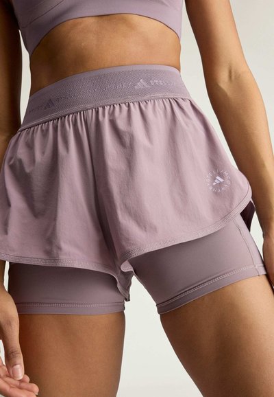 Woman wearing mauve two-in-one athletic shorts with fitted inner layer and loose outer layer, featuring Stella McCartney logo on the outer shorts.