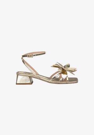 Sandals featuring a metallic gold finish, square toe, and a low block heel. The design includes multiple straps and a large floral accent.