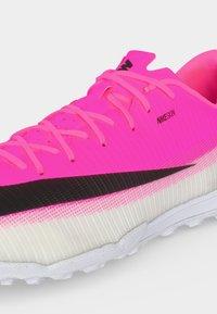 Φωτεινό ροζ αθλητικό παπούτσι Nike με μαύρο σήμα, ροζ κορδόνια, κείμενο "NIKESKIN" και υφασμένο λευκό πάτο σε ουδέτερο φόντο.