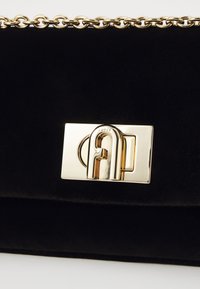 Sac en velours noir avec une chaîne dorée et un fermoir rectangulaire doré proéminent avec un logo texturé.