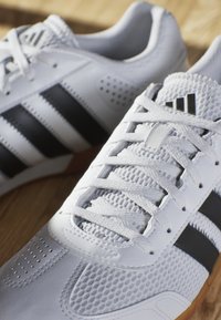 Baskets de sport blanches avec des rayures noires, dotées d'un dessus en maille texturée, d'accents en cuir lisse et d'un système de laçage traditionnel.