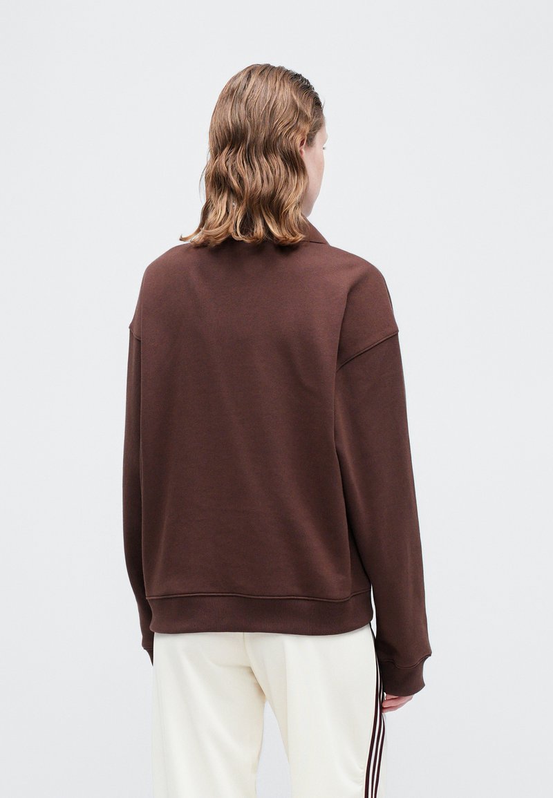 Sweat-shirt marron avec une coupe décontractée, des poignets et un ourlet côtelés. Tissu doux, design minimaliste et un petit détail de col.
