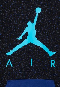 Svart tyg med ett prickigt mönster har en ljusblå silhuett av en basketspelare och ordet "AIR" i blått under.