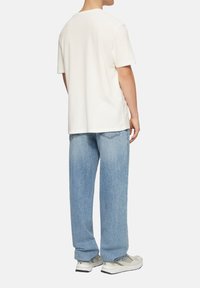 Weißes T-Shirt mit kurzen Ärmeln, kombiniert mit hellblauen, bequemen Jeans. Die Sneaker haben ein grau-weißes Farbschema mit Mesh- und Gummielementen.