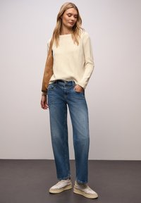 Kremowy sweter, jasnoniebieskie jeansy o prostych nogawkach oraz beżowe tenisówki. Sweter ma fakturowane wykończenie; jeansy posiadają przednie kieszenie i efekt wyblaknięcia.