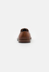 Scarpa in pelle marrone con finitura texturizzata, punta arrotondata e tacco in legno basso. Il retro presenta un dettaglio di cucitura sottile.