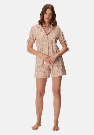 Woman standing barefoot wearing a light pink short-sleeve button-up shirt and matching shorts with a subtle leopard print pattern.
