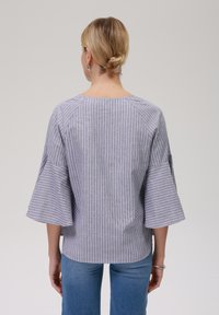 Rutet blouse i grå og hvit bomull, med rund hals og flagrende ermer. Bakfra vises raglan-sømmer og en avslappet passform.