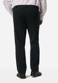 Černé kalhoty s přímým střihem, které mají dvě zadní kapsy se zapínáním na knoflíky, nošené s hnědými botami. Materiál vypadá hladce a pevně.