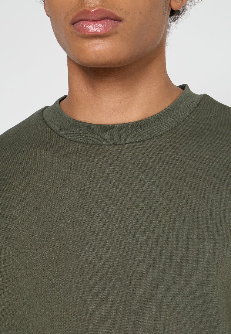 Olijfgroen katoenen jersey t-shirt met een ronde hals en korte mouwen. Soepele textuur en een eenvoudig, strak ontwerp zonder versieringen.