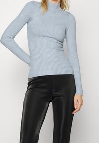 Chemise à manches longues à col roulé côtelé bleu clair, design ajusté avec un motif texturé, associée à des leggings noirs brillants.