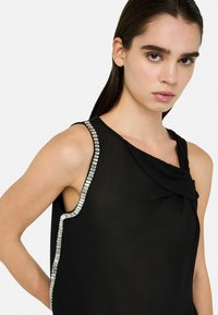 Black sleeveless top with a draped neckline and a textured silver trim along the armhole, featuring a smooth and lightweight fabric.