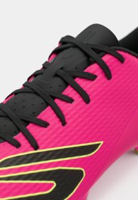 Bright pink soccer cleat with a textured surface, black laces, and a black and neon yellow accent logo on the side.