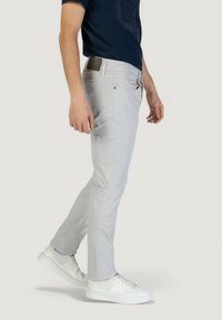 Pantalones gris claro en corte ajustado, con bolsillos laterales y un acabado texturizado sutil, combinados con zapatillas blancas.