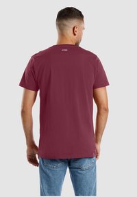 Burgunderfarbene Baumwoll-T-Shirt mit kurzen Ärmeln, Rundhalsausschnitt und kleinem weißen Markenlogo auf dem oberen Rücken. Glatte Textur und normale Passform.