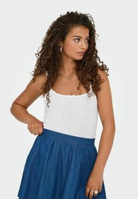 Top senza maniche lavorato a maglia bianca con scollo a scallop e spalline sottili, abbinato a una gonna di jeans blu con vita arricciata.