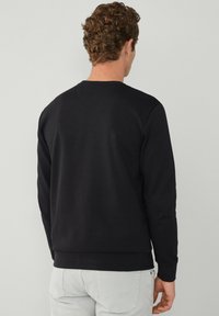 Sweat-shirt noir avec un col rond, des manches longues et un tissu texturé. Poignets et ourlet côtelés. Design minimaliste, sans embellissements visibles.