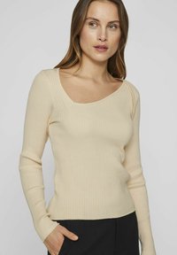 Maglietta a maniche lunghe color crema a coste con scollatura ampia e silhouette aderente, caratterizzata da una texture morbida e un lieve elastico.