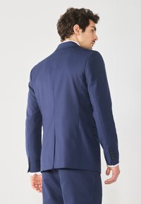 Chaqueta de traje azul marino que presenta un diseño estructurado con un ajuste a medida, costuras detalladas y acentos de botones en las mangas. Vista trasera mostrada.