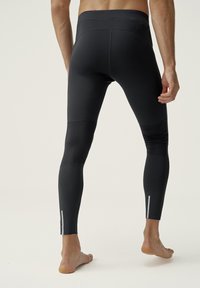 Černé sportovní legíny s vysokým pasem, vyrobené z hladkého materiálu, s kontrastními panely a reflexními detaily na kotníku.