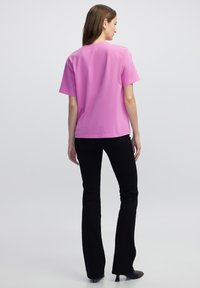 Strak aansluitend, t-shirt met korte mouwen in felroze katoen, met een ronde hals en een gladde textuur. Gecombineerd met uitlopende zwarte broek en zwarte hakken.