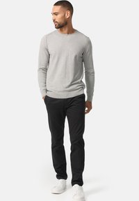 Grey long-sleeve sweater with ribbed neckline, paired with black pants and white sneakers. The outfit features a relaxed fit and minimal design.