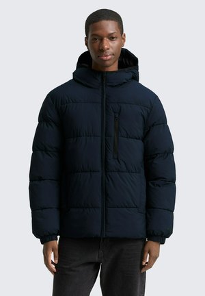Marine blauwe pufferjas met capuchon, gekwilt ontwerp, vooraan met ritssluiting en een zak op de linkerborst. Bevat elastische manchetten voor een snug fit.