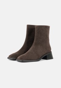 Stivaletti alla caviglia in suede marrone con punta arrotondata e tacco a blocco. Texture liscia, design minimalista e assenza di hardware o dettagli visibili.