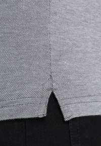 Šedá strukturovaná tkanina se bočním rozparkem. Materiál je tkaný, s jemným vzorem, který se nachází vedle černé tkaniny.