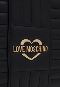 Svart handväska med quiltat mönster som har en gyllene "LOVE MOSCHINO"-logotyp i hjärtform, centrerad på en panel.