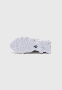 Semelle de chaussure de sport blanche en caoutchouc texturé, présentant des motifs circulaires et en zigzag, garantissant adhérence et durabilité.