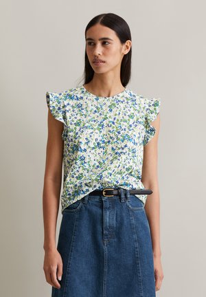 Floral-patterned blouse in white, featuring blue and green flowers, short flutter sleeves, and a round neckline. Paired with a denim skirt.