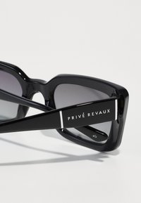 Svarta oversized solglasögon med gradientgrå linser, rektangulär form, glänsande acetatram och logotypdetaljer vid skalmen.