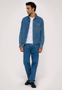 Jeansjacka och jeans i mellanblått. Jackan har en bröstficka med emblem, knappstängning och klassisk krage. Vit t-shirt under.