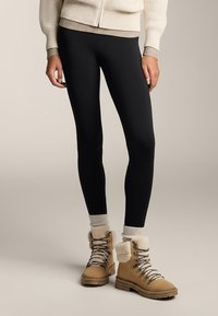 Crne tajice uparene s bež čizmama na vezanje, s krznom obloženim rubom i sivim čarapama. Gornji dio je kremasto pleteni džemper.