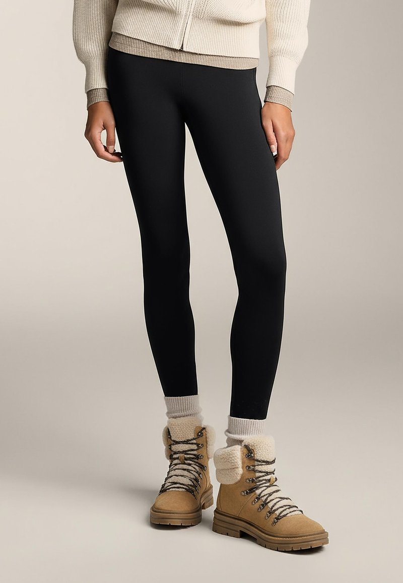 Crne tajice uparene s bež čizmama na vezanje, s krznom obloženim rubom i sivim čarapama. Gornji dio je kremasto pleteni džemper.