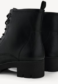 Paire de bottines en cuir noir avec fermeture à lacets sur le devant, talons carrés épais, coutures décoratives et languettes à l'arrière pour un enfilage facile.
