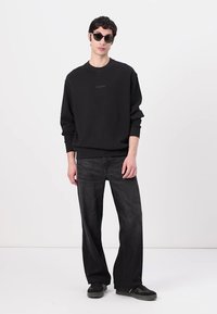 Sort sweatshirt med rund halsudskæring, parret med løstsiddende mørke jeans og sorte sneakers. Modellen bærer runde sorte solbriller.