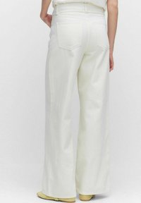 Vita vida byxor med hög midja och slät yta, två bakfickor, i kombination med en ljus topp och neutrala skor.
