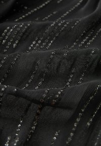 Tissu noir à texture douce avec des rayures métalliques argentées et des sequins, créant un motif scintillant sur toute la surface.