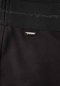 Schwarzer Stoff mit strukturierter Oberfläche, versehen mit einem silbernen Metall-Tag "Street One" und kontrastierenden Nähten oben.