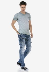 Lichtgroene, korte mouwen V-hals T-shirt gecombineerd met vervaagde blauwe cargobroek met meerdere zakken en ritsaccenten, afgewerkt met zwarte sneakers.
