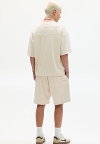 Chemise à manches courtes en maille beige et shorts assortis, coupe décontractée, tissu texturé, avec poches latérales, assortis avec des baskets blanches et brunes.