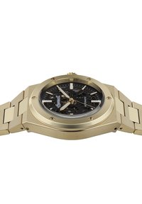 Gouden horloge met een hexagonale kast, zwart skelet-dial en gouden accenten. De metalen armband heeft rechthoekige schakels en een geborstelde textuur.