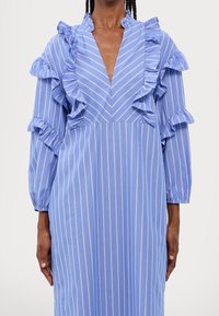 Blårandig klänning med volanger längs halsringningen och ärmarna, med djup V-hals och lättviktsmaterial.