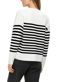 Weißer Pullover mit horizontalen schwarzen Streifen, gerippter Textur, angeschnittenem Schulterdesign und einem leicht gekürzten Rücken. Schwarze Jeans sind darunter sichtbar.